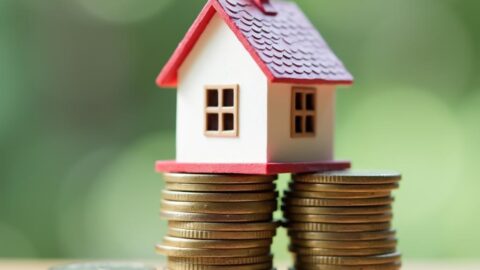 A small house model on top of a stack of coins, symbolizing real estate investment with limited funds.